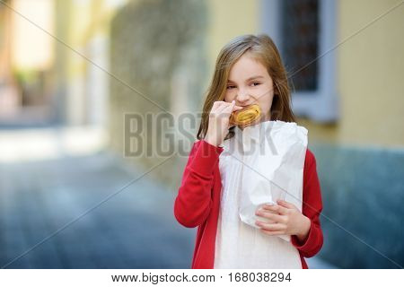 Adorable Little Girl Eating Fresh Baked Bun On Warm And Sunny Summer Day