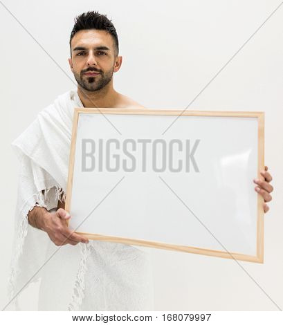 Muslim man posing as ready for Hajj visiting Kaaba in Mecca holding white board for copy space your text or image