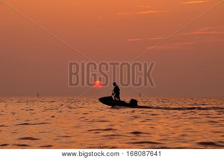 Silhouette of man driving jetski on the sea with during sunset