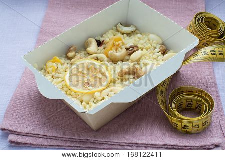 bulgur with nuts decorated with the dihydrogenated lemon in a craft box on a on a linen cloth with a centimetric tape. Healthy nutrition dish.