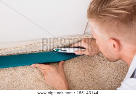 Close-up Of A Young Handyman Cutting Installing Carpet With Cutter