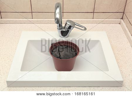 Water shortage concept. Pot with dry ground in white sink
