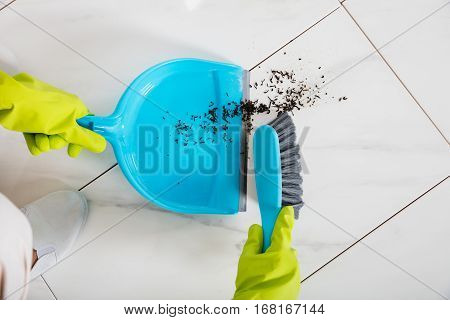 Close-up Of Person Wearing Gloves Sweeping Floor With Broom And Dustpan