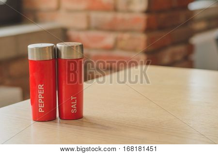 Red plastic salt cellar and pepperbox on a wooden table on loft brickwall background faded colors