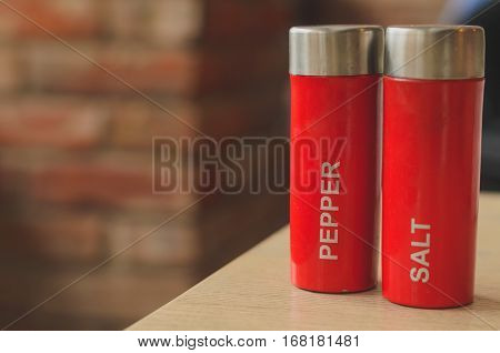 Red plastic salt cellar and pepperbox on a wooden table on loft brickwall background faded colors