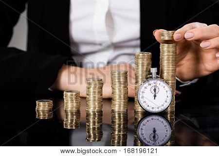 Businesswoman Stacking Coins With Stopwatch In Front On Desk. Quick Money Concept