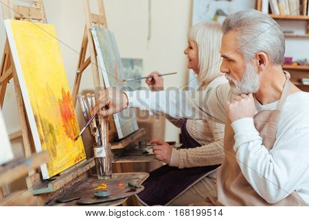 Sweet cooperation. Delighted talented concentrated colleagues drawing a picture while spending time in painting class and working as artists.