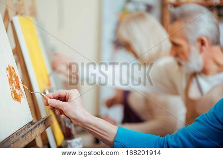 Productive cooperation. Concentrated artists working together in painting studio while holding brushes and enjoying their hobby.