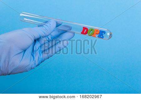 Word dope of colored wooden letters in test-tube. Hand in glove holding a test tube on a blue background