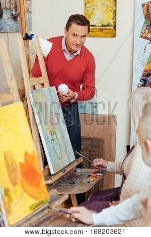 Interesting process. Overjoyed handsome young man teaching people and spending time in painting studio while helping them to draw.