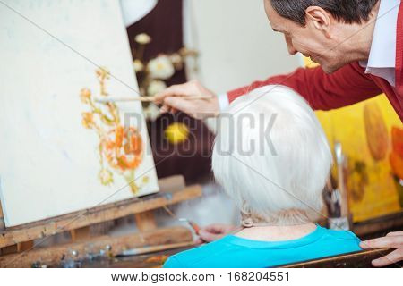 Nice learner. Talented young concentrated artist teaching elderly woman while drawing and spending time in painting school.
