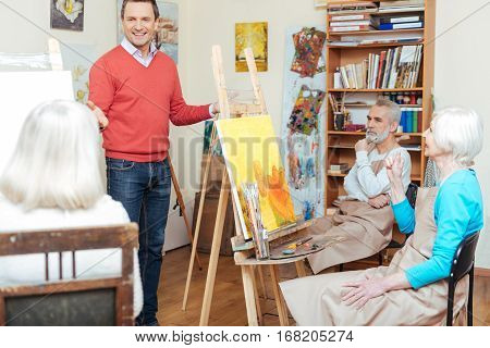 Interesting information. Handsome talented young artist lecturing and gesturing while working in painting school.