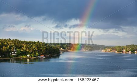 panorama of green coast of Baltic Sea with villages and rainbow over water in sunny autumn day Sweden