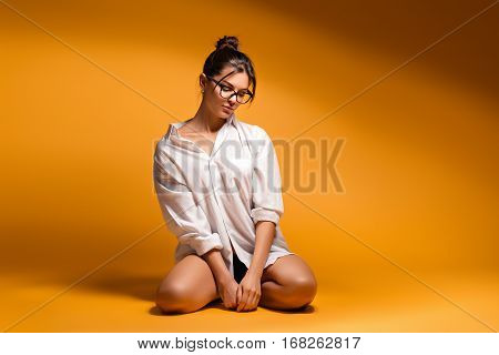 A young girl kneeling. Young pretty beautiful emotional girl in glasses posing on a yellow background. A woman stand on a knees. Young girl sitting on a knees. woman sitting on a knees.