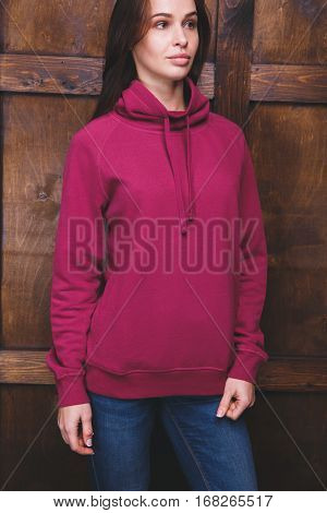 Young woman wearing blank magenta sweatshirt with area for your logo or design, mock-up of template magenta sweatshirt, wooden wall in the background
