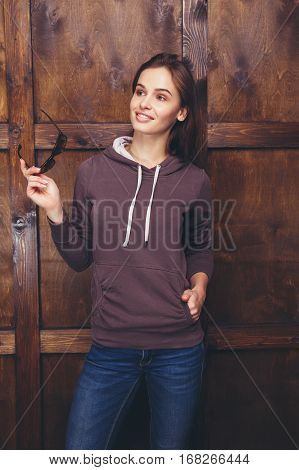 Young woman wearing blank brown sweatshirt with area for your logo or design, mock-up of template brown sweatshirt, wooden wall in the background