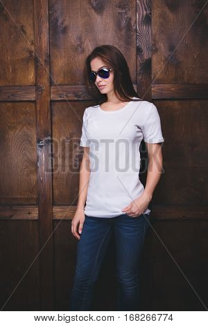 Young woman wearing blank white t-shirt with area for your logo or design, mock-up of template white t-shirt, wooden wall in the background