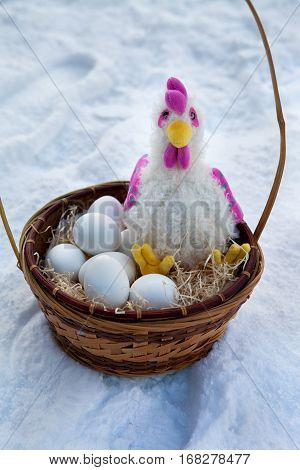 Basket with paraphernalia on Easter rooster and Easter eggs lying in basket in the snow.