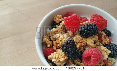 A white bowl filled with granola, raspberries, blackberries and yogurt.