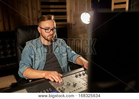 music, technology, people and equipment concept - man at mixing console in sound recording studio