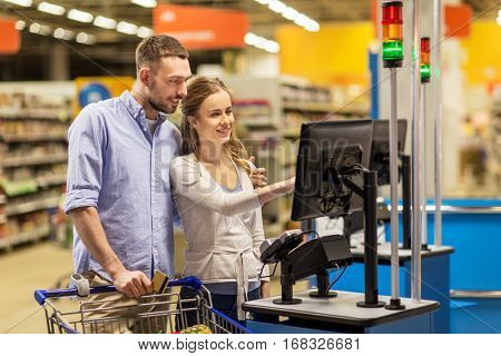 shopping, sale, payment, consumerism and people concept - happy couple with bank card buying food at grocery store or supermarket self-service cash register