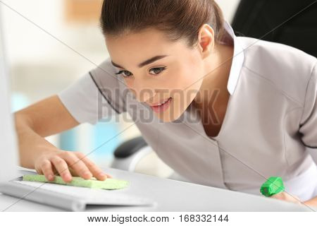 Beautiful young charwoman wiping dust in office, closeup