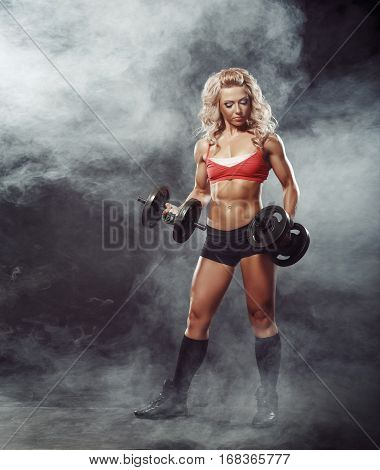photo of athletic young blondy curl girl doing a fitness workout with dumbbells on smoke background