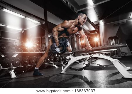 Athlete muscular bodybuilder training hands with dumbbells in gym
