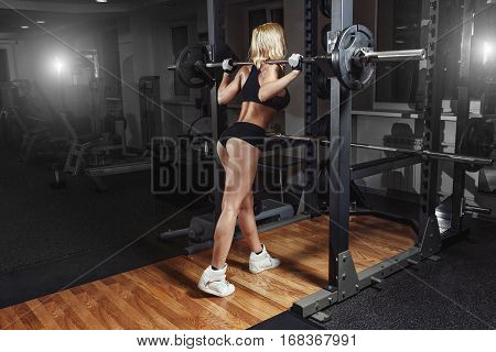 Young sexy girl in the gym doing squat with barbell in training machine
