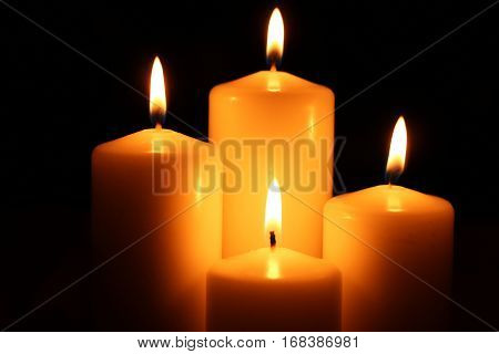 Four big different burning candles. Bright light on dark background. Romantic or RIP darkness template.