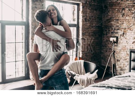 Loving him so much! Beautiful young couple enjoying free time at home while attractive woman embracing handsome man and smiling