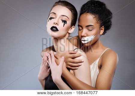 I hold you. Creative good looking graceful girls acting as opposite yin and yang and wearing corresponding looks while working on a conceptual project in a studio