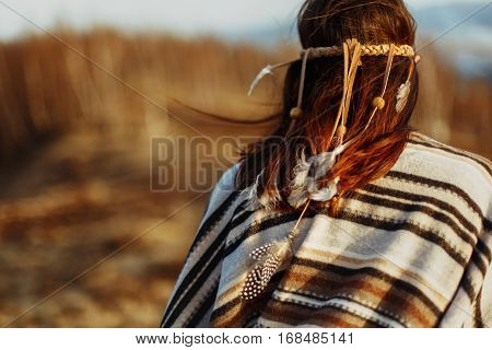 Back Of Native Indian American Woman Walking In Mountains In Evening, Hair With Feathers