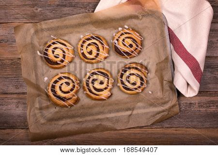 Overhead view of freshly baked cinnamon buns on greaseproof paper, with tea towel and old wood background. 