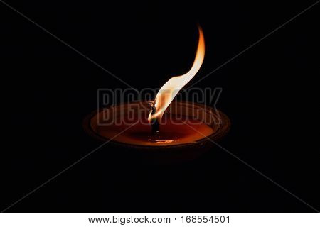 Burning fire in wax candle cup on lowkey black scene.