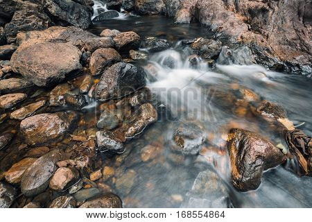 Moving stream water flowing through brown rock river path in rain forest.
