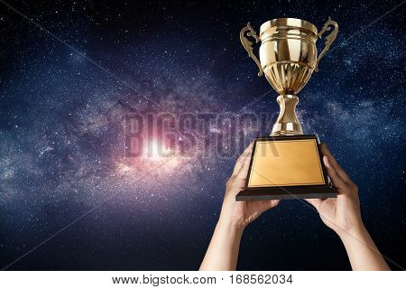 a man holding up a gold trophy cup with milky way sky background copy space ready for your trophy design.