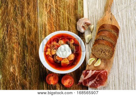 Red vegetable soup in the white plate and bread. On a wooden background.