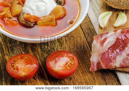 Red vegetable soup in the white plate and bread. On a wooden background.