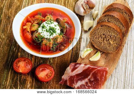 Red vegetable soup in the white plate and bread. On a wooden background.
