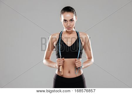 Young Sporting woman with skipping rope looking at camera. Isolated gray background