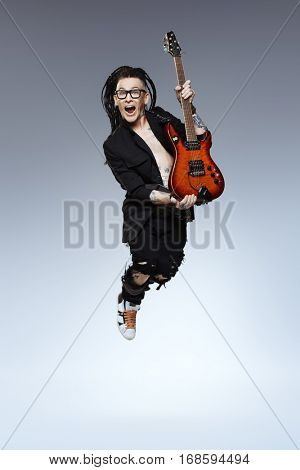 Entertainment and musical concept. Excited rock musician is jumping with his electrical guitar. Full length studio shot. 