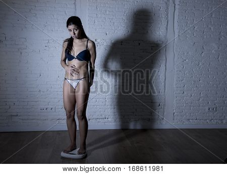 young fit and slim woman or teenager girl checking body weight on scale with big edgy shadow light sad desperate and frustrated in anorexia and bulimia nutrition disorder and overweigh obsession