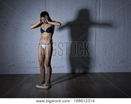 young fit and slim woman or teenager girl checking body weight on scale with big edgy shadow light sad desperate and frustrated in anorexia and bulimia nutrition disorder and overweigh obsession
