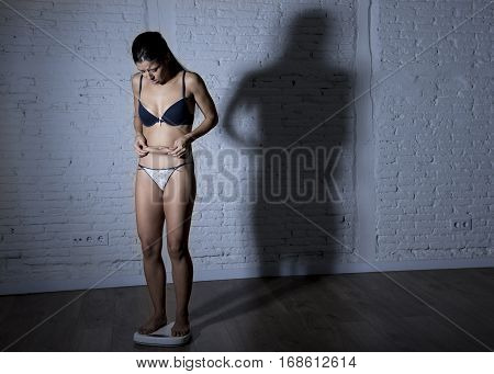 young fit and slim woman or teenager girl checking body weight on scale with big edgy shadow light sad desperate and frustrated in anorexia and bulimia nutrition disorder and overweigh obsession