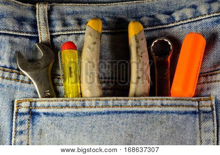 Different hand tools in a pocket of the blue jeans