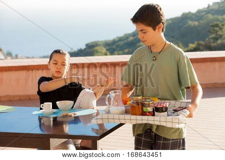 Satiates girl refuses breakfast, boy with a tray with many jams in the foreground