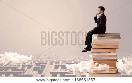 A serious businessman in suit sitting on a pile of giant books in front of a grey wall with clouds, labirynth