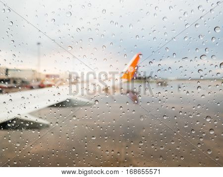 Abstract defocused blur of airplane at airport with sunset after the heavy rain. -Focus on raindrops windows glass.