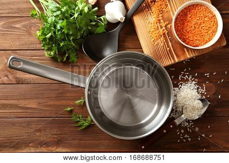 Stainless saucepan, parsley and lentil on wooden background